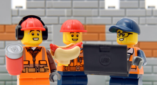 Lego minifigures of workers in redheads and engineer with laptop against a brick wall. Editorial illustrative image of popular children toys and people occupation.