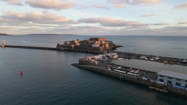 St Peter Port Harbour Guernsey flight over Albert Pier and model yacht pond towards Castle Cornet in golden hour with distant views of Sark and calm blue sea