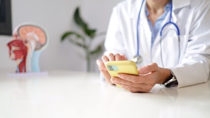 Medical professional wearing a white lab coat using a smartphone for telehealth communication and digital health services in a clinic, accessing patient information © NJF