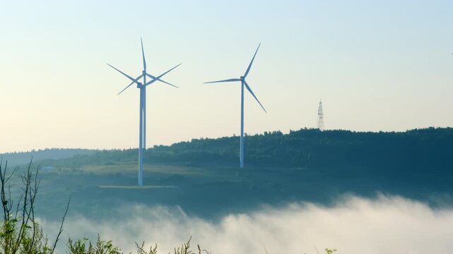 Wind farm generators with huge propellers on hill over hazy valley. Windmills use renewable natural source to produce clean power on mountain
