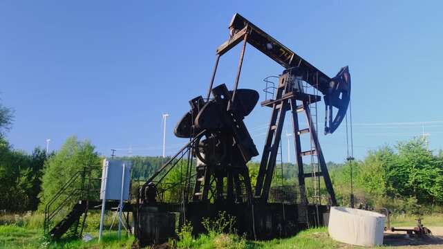 Old oil well pumps fossil oil against wind turbines at countryside slow motion. Transition to renewable power sources and environment conservation