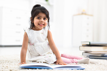 Fototapeta premium Cute little girl reading book on floor at home. Space for text