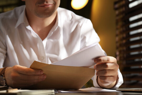 Man putting letter into envelope at wooden table indoors, closeup