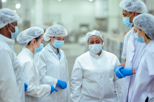 Multinational factory workers stand together in discussion before starting production shift in canned fish facility. Scene shows planning, teamwork, hygiene protocol for efficient food manufacturing.
