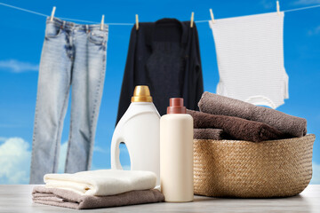 Laundry basket with clean towels and bottles of detergent on table. Clothes drying against sky