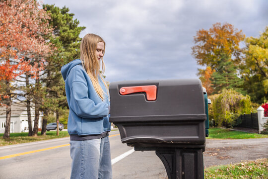 Young woman checking mailbox on suburban street under dramatic autumn sky