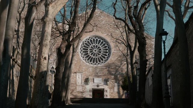 Symmetrical view of the Romanesque facade of San Giusto Cathedral in Trieste Italy framed by tall trees with the stone rose window and main entrance portal