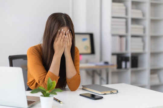 Stressed professional woman at her desk covering her face with hands, overwhelmed and exhausted from office work, symbolizing anxiety, burnout and workplace pressure