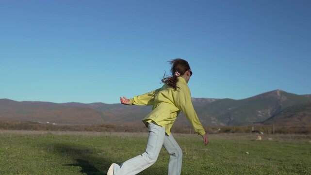 Girl acrobatics mountain Young female child performs gymnastics and plays in a sunny green field with massive forested mountains in the background.