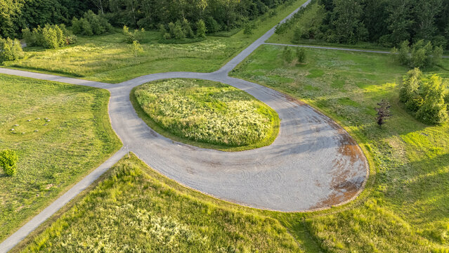 Aerial view of a roundabout surrounded by vibrant green grass and trees, paths extending outwards, all basking in the soft light of the day, De Kiem, Flevoland, Netherlands.