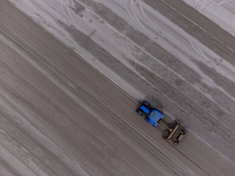 Aerial view of a lone blue tractor carving precise lines in the muted earth, creating a stark contrast against the vast landscape, Almere, Flevoland, Netherlands.