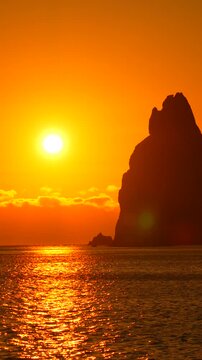 Sunset ocean rock island silhouette glowing against an orange sky over the sea