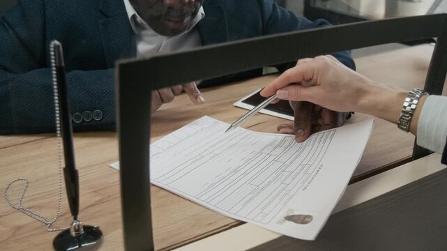 Medium close-up of 50-year-old African American businessman asking questions on correct filling of visa application form to unrecognizable female consular officer at foreign embassy
