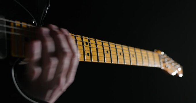 Dimly lit close-up of a musician&rsquo;s hand pressing strings on an electric guitar fretboard, highlighting texture, precision, and the expressive mood of live music performance
