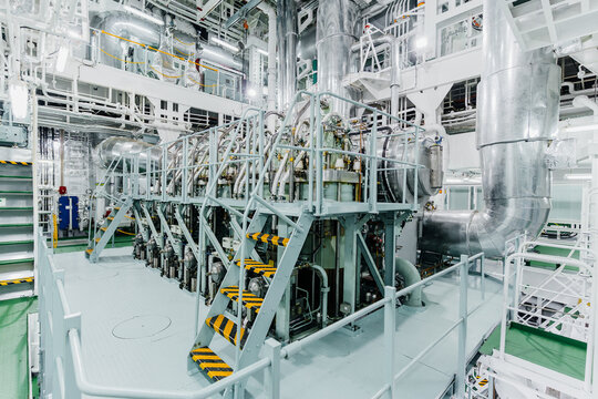 High angle interior view of a massive marine diesel engine inside a ship engine room with complex industrial piping