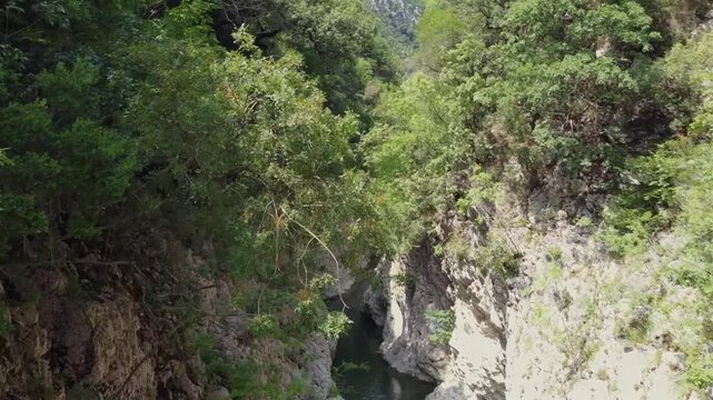 Cinematic drone shot over the legendary Acheron river. High-angle view showing the narrow passage between steep rocky cliffs and lush green forest. Ideal for adventure and nature documentaries.