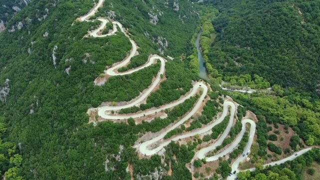 Cinematic drone shot of the famous winding road with hairpin turns in Papigo. High-angle view of the zig-zag route through lush green forest in Epirus. Perfect for travel and automotive films.