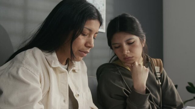 Tilting medium close-up of busy, frowning mature Hispanic woman and young girl completing visa application forms at foreign consulate, for immigration, citizenship, tourism or study abroad