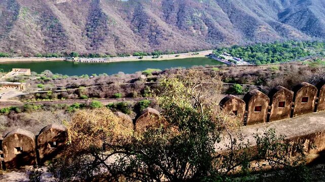 Showing view of Maota Lake and Amer Fort from Nahargarh Fort, with old fort battlements in foreground, winding defensive walls along hillside, and Aravalli mountains in background.