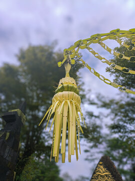 Balinese Penjor Bamboo Decoration with Janur Palm Leaves Hanging Over Traditional Gate, Cultural Ritual Ornament in Tropical Garden, Indonesian Heritage Festival Symbol