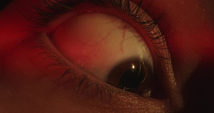Macro shot of a woman eye, in red light, pupils dart fearfully from side to side. Concepts related to medicine and ophthalmology, eye health, psychology, fatigue, stress, diseases, and horror themes