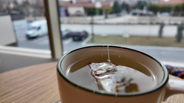 Ultra slow motion 4K video of a tea bag in a cup of herbal tea, gently steeping in hot water, steam rising, soft natural light, shallow depth of field, cinematic, warm tones, calm atmosphere