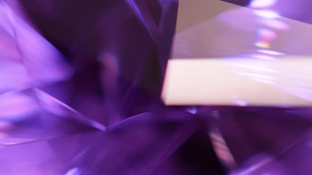 Slow motion macro tracking dolly of amethyst crystal facets rotating and refracting light with glossy purple reflections in studio tabletop setting