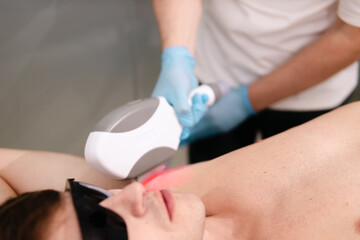 Naklejka premium Person receiving laser hair removal treatment, a specialist holding a modern laser device applying advanced aesthetic medicine technology to body for permanent hair reduction