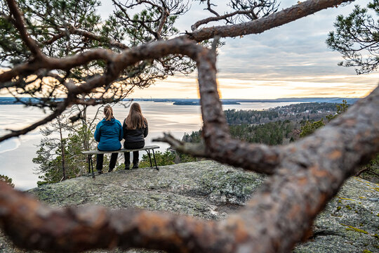 Rear view of mother and daughter sitting on hill while looking at view seen between branch