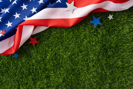 Wavy American flag and glitter stars laid on green grass evoking patriotism, summer holidays, and national pride for Independence Day, Memorial Day, Labor Day and other USA celebrations
