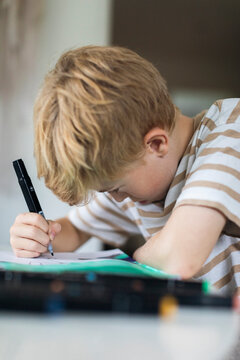 Focused boy coloring in book with felt tip pen at home
