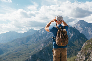 A male hiker with a backpack stands on a hill looking at a majestic mountain range. This scene captures the spirit of adventure, freedom, and active exploration in the great outdoors. © magic_cinema