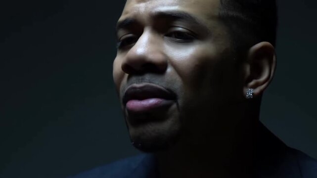 Slow motion tracking shot of male singer close up turning head while singing in dark studio portrait with low key dramatic lighting