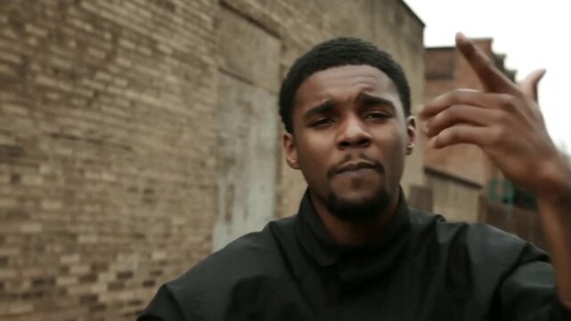 Tracking handheld shot of young man rapping and gesturing in brick alleyway backstreet urban setting during overcast daytime