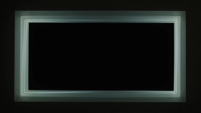 Slow motion pan of illuminated rectangular border with light sweep across dark interior wall in minimalist studio