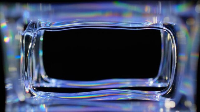 Tracking slow motion of clear glass rectangle refracting light through hollow opening on black studio background