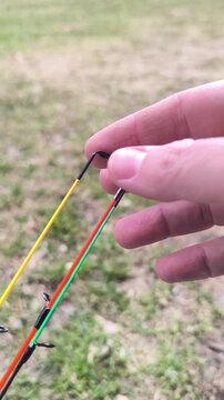 Close up of an angler hand bending three colorful fishing rod tips to demonstrate different thickness and flexibility outdoors