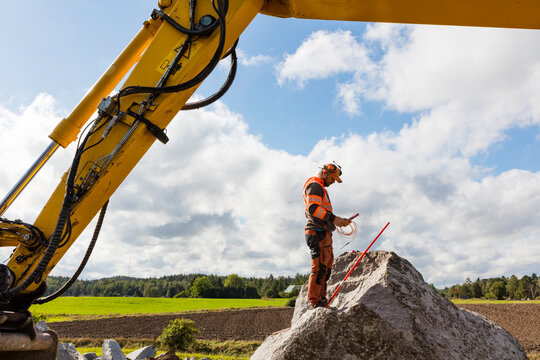 Full length of construction worker standing on rock against cloudy sky