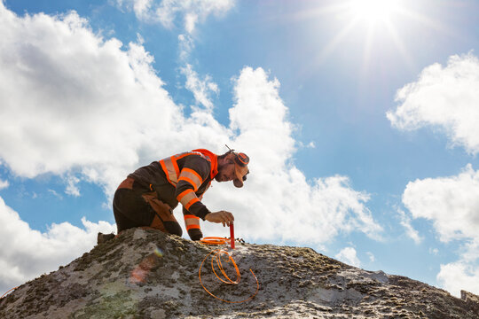 Low angle view of construction worker marking on rock against cloudy sky at sunny day