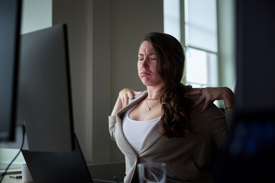 Tired businesswoman stretching her back while sitting at desk in tech office
