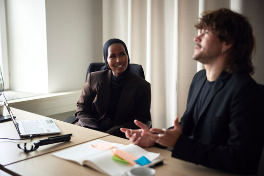 Male entrepreneur discussing ideas with female colleague sitting in office