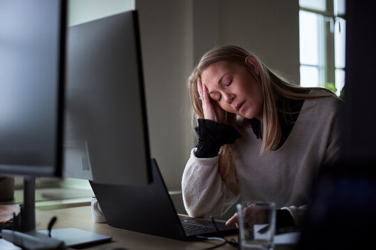 Exhausted female entrepreneur with eyes closed leaning on elbow in tech office