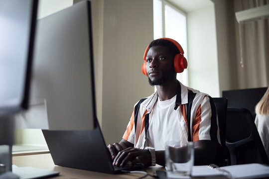 Concentrated male programmer wearing wireless headphones working on technologies in office