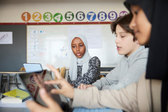 Group of students using laptops while studying together in classroom at school