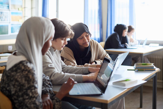 Group of focused students using laptops while sitting at desk in classroom
