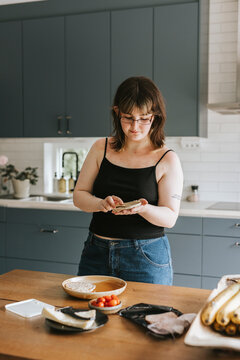 Young woman making breakfast while standing near table in kitchen at home