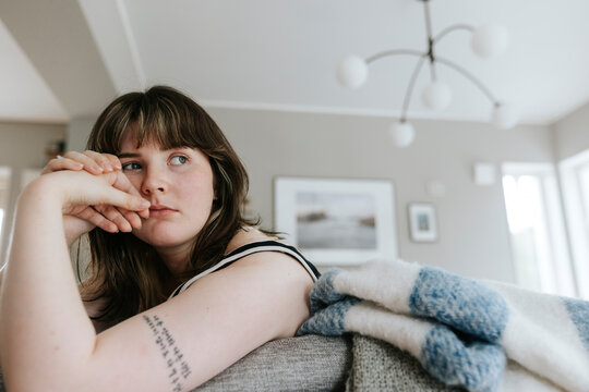 Thoughtful young woman leaning on sofa in living room at home