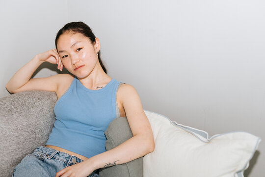 Portrait of beautiful young woman sitting on sofa while leaning on elbow at home