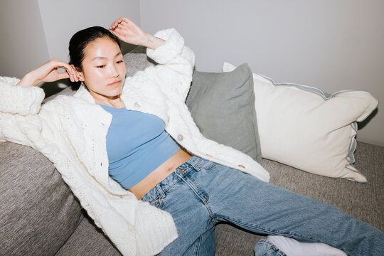 High angle view of young woman wearing jacket lying on sofa at home