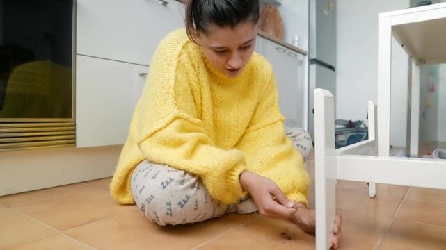 Woman Searches Floor. Young Woman On Tiled Floor Carefully Seeking Tiny Missing Item Near Furniture Leg